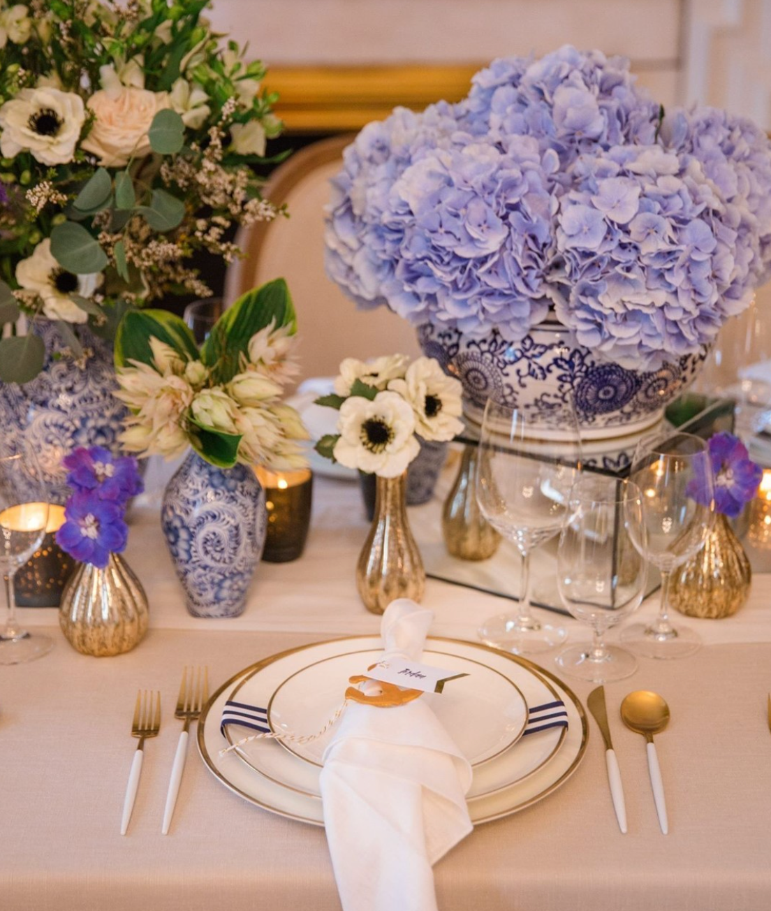 WhiBrushed Gold Coupe Chargers styled with blue hydrangeas, gold flatware, and layered white dinnerwarete and brushed gold charger plates layered beneath fine dinnerware at an outdoor estate wedding reception.