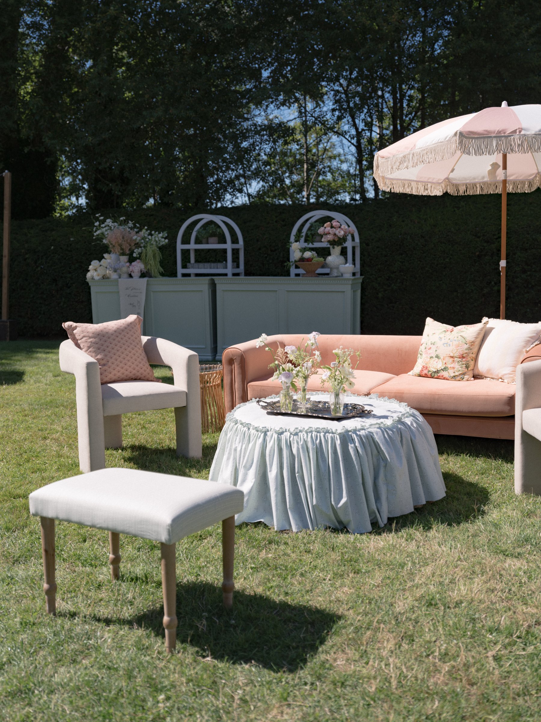 Luxury garden wedding lounge featuring light sage green gathered slip cover and ottoman with vintage silver serving tray and floral styling