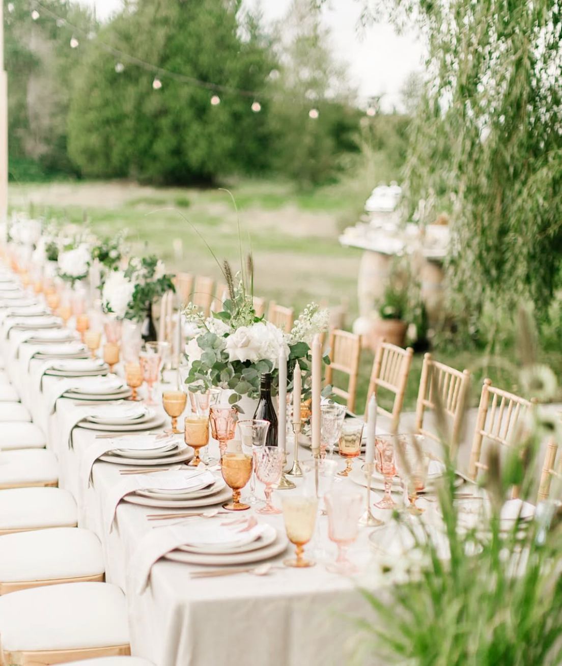 Vintage blush and amber glassware styled on an elegant outdoor wedding reception table with romantic floral centerpieces.