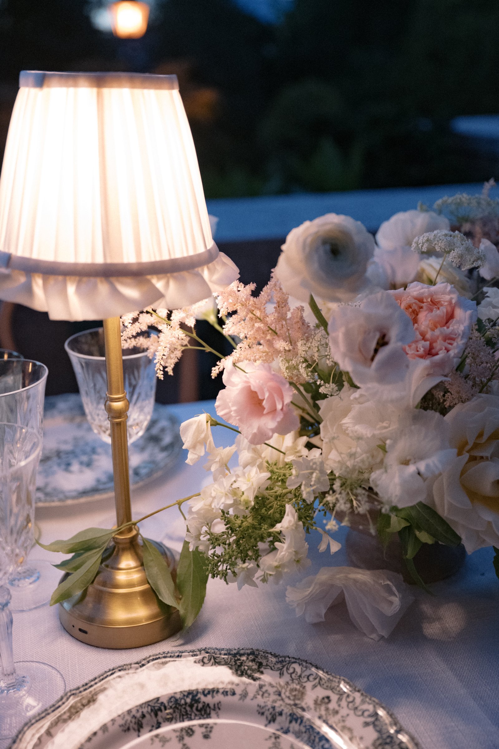 Close-up of a brass table lamp with crème ruffled shade beside romantic floral arrangements on a luxury wedding reception table.