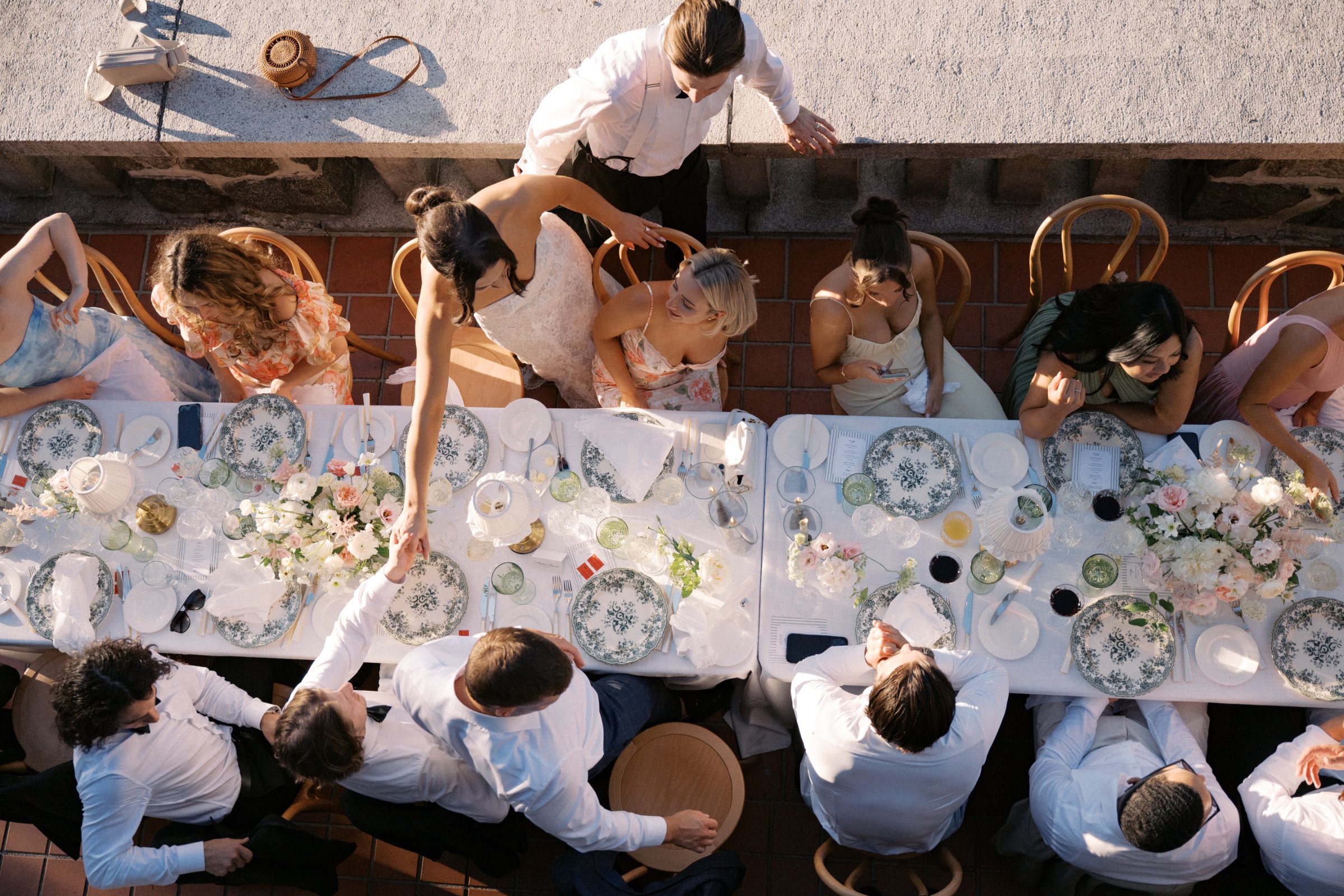 Guests gathered around an elegant outdoor reception featuring brass table lamps with crème ruffled shades, layered linens, floral arrangements, and candlelight.