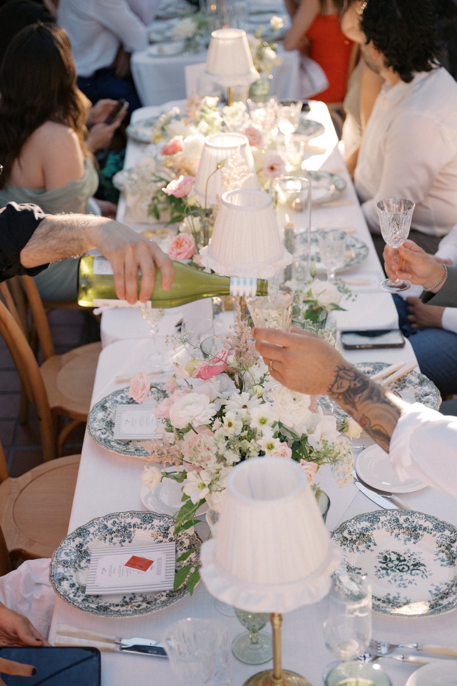 Guests celebrating at an elegant reception featuring brass table lamps with crème ruffled shades and romantic floral décor.