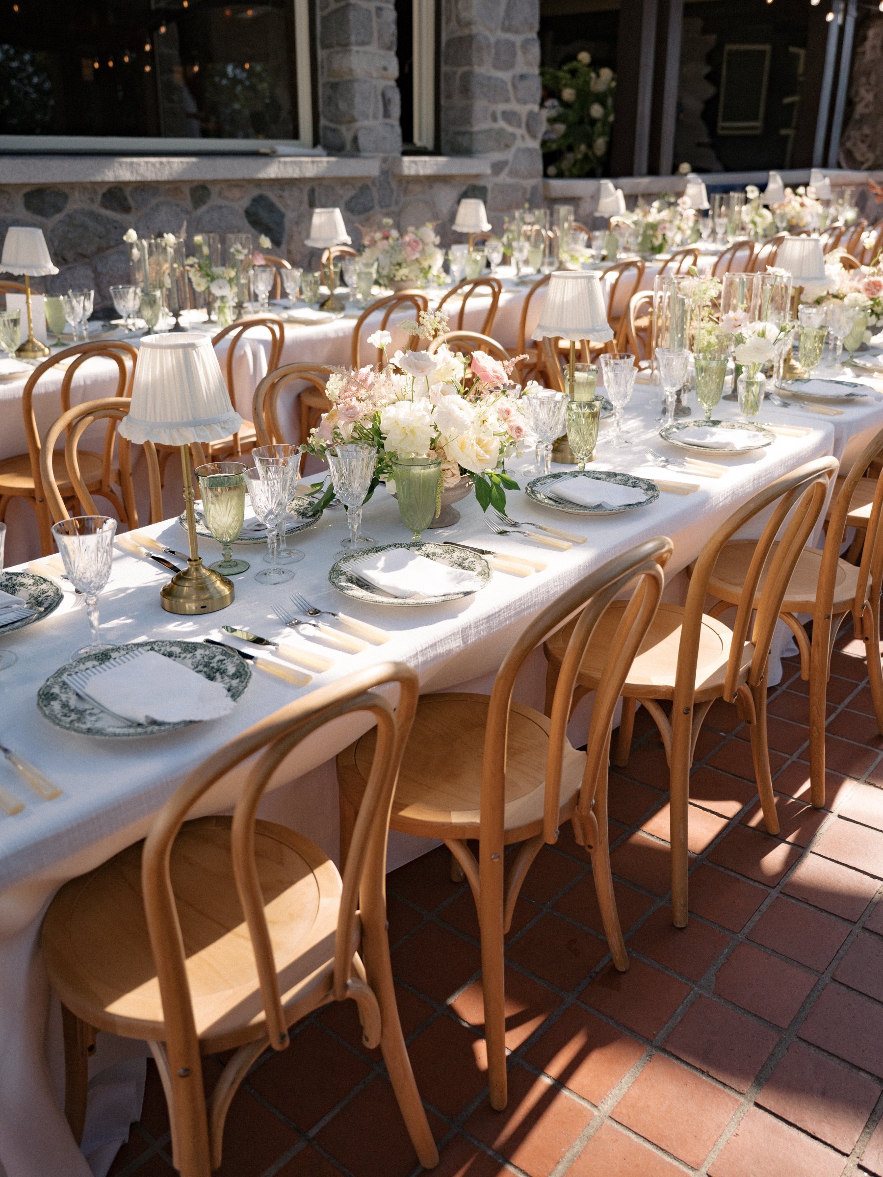 Long reception table featuring brass table lamps with crème ruffled shades, layered place settings, and romantic floral arrangements.