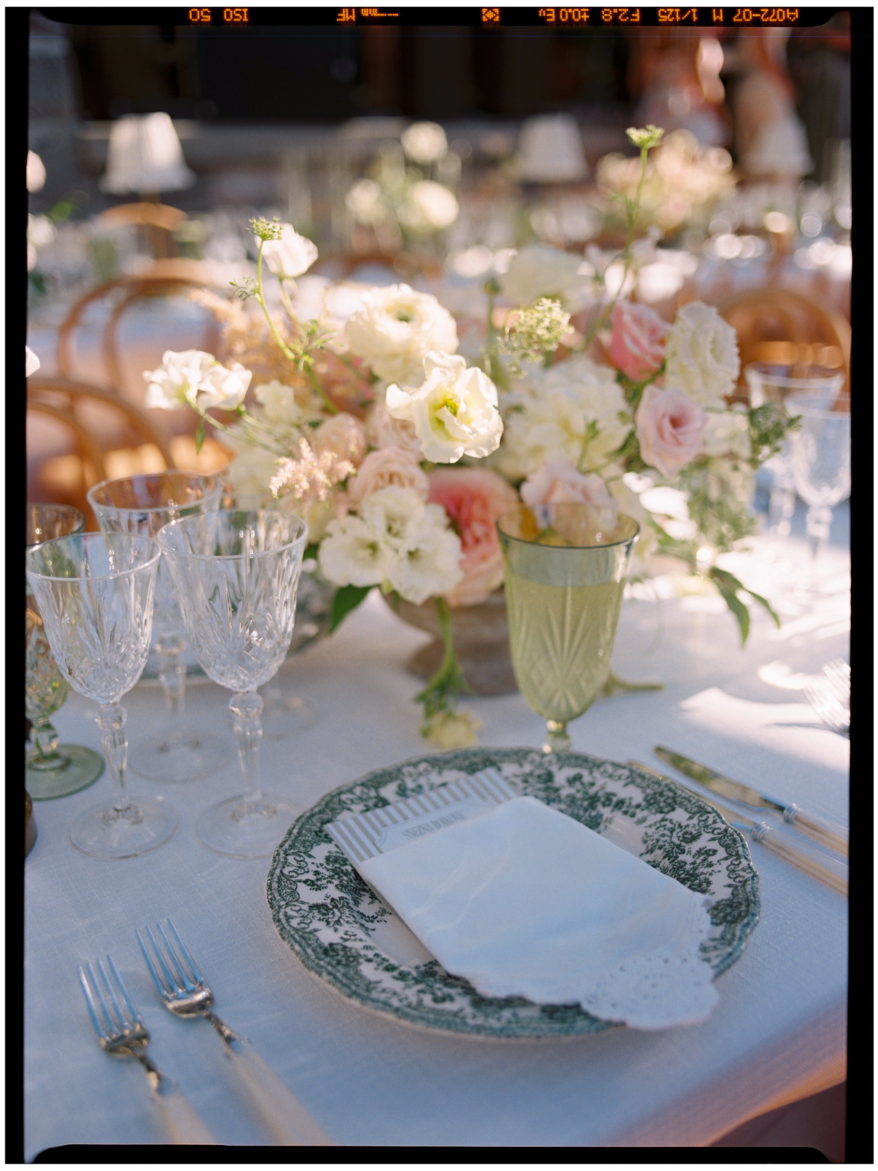 Crystal red wine glasses styled on an elegant wedding table with soft florals, layered china, and candlelight.