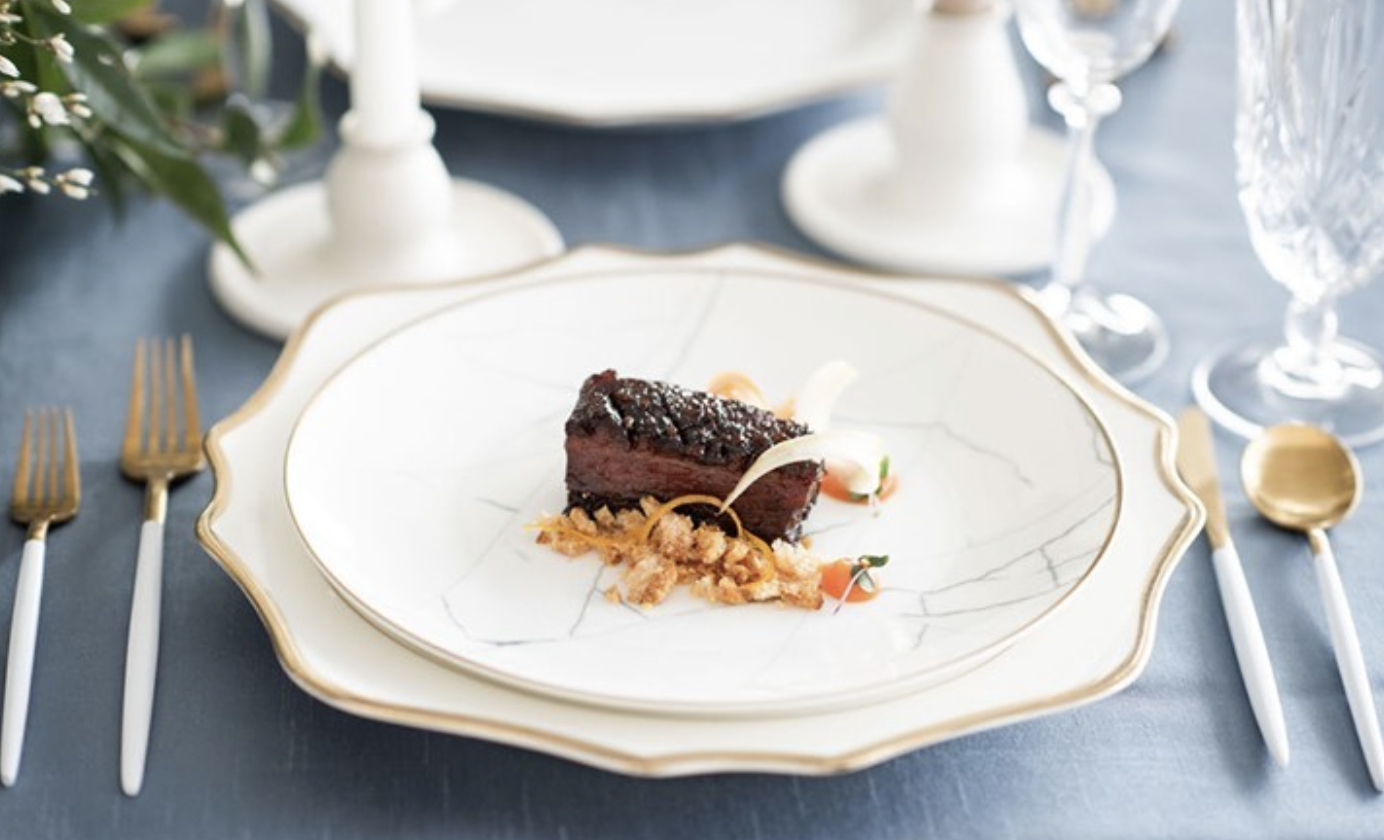 Anna Weatherly White & Gold Charger plates styled with layered dinnerware, gold flatware, elegant menus, and crystal glassware for a luxury wedding reception.