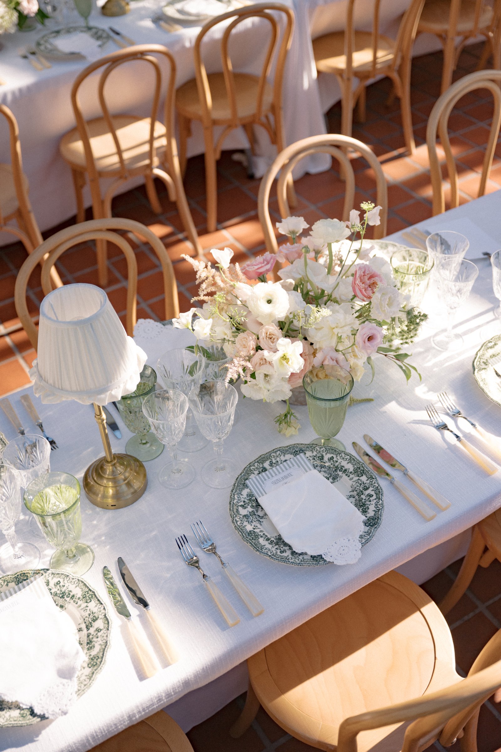 Brass table lamp with crème ruffled shade styling an elegant wedding reception tablescape with layered linens, florals, and fine dinnerware.